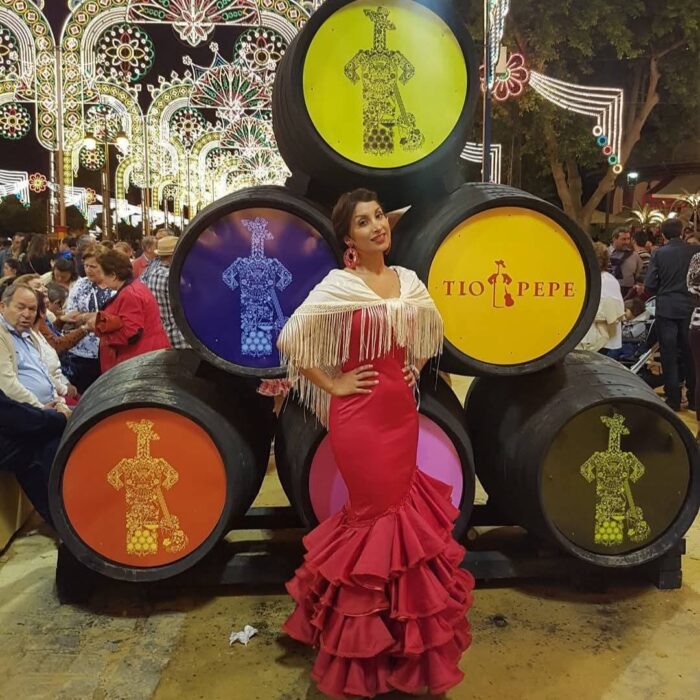 Mujer vestida de sevillana con vestido rojo y mantón blanco en la Feria de Jerez frente a barriles de Tío Pepe