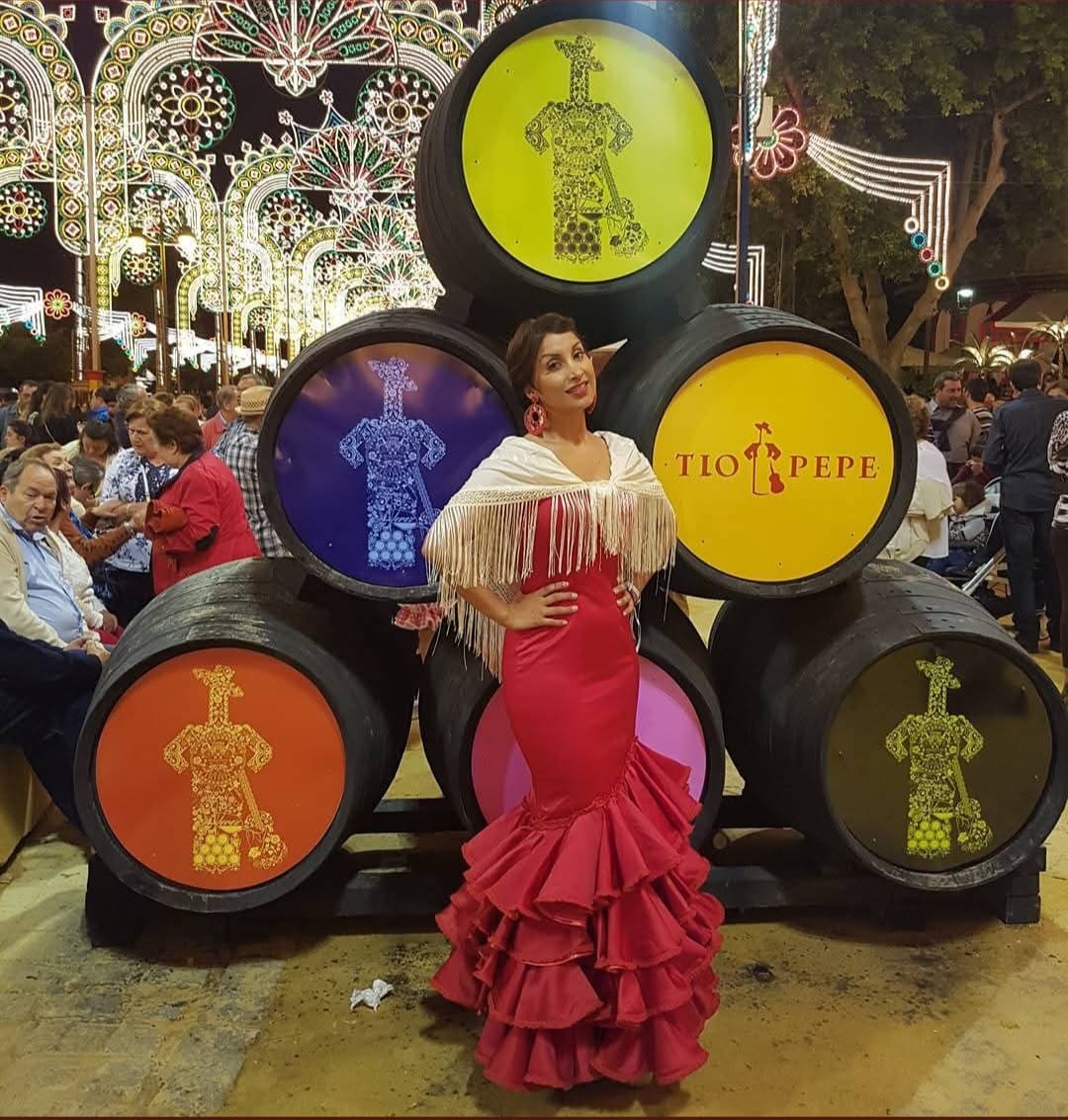 Mujer vestida de sevillana con vestido rojo y mantón blanco en la Feria de Jerez frente a barriles de Tío Pepe