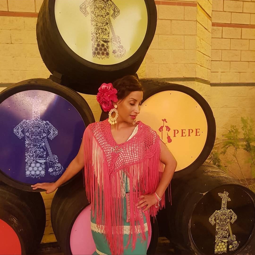 Vestido verde de sevillanas con mantón rosa en la Feria de Jerez junto a los barriles del Tío Pepe