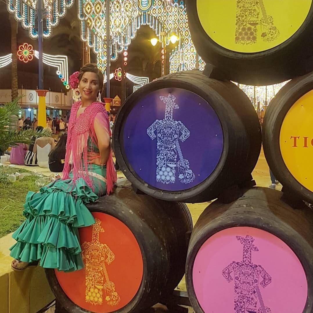 Mujer con traje tradicional de sevillana verde y mantón rosa sentada en barriles del Tío Pepe en la Feria de Abril